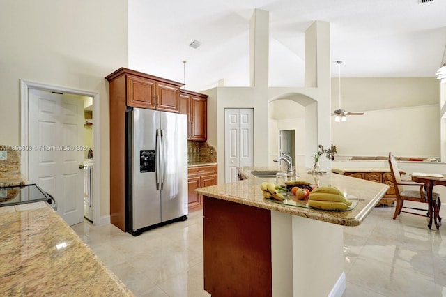 kitchen featuring stainless steel fridge, tasteful backsplash, sink, high vaulted ceiling, and light stone counters