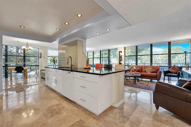 kitchen with a notable chandelier, white cabinetry, floor to ceiling windows, white dishwasher, and sink