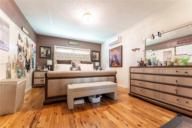 bedroom with a textured ceiling, a wall mounted air conditioner, and light hardwood / wood-style floors