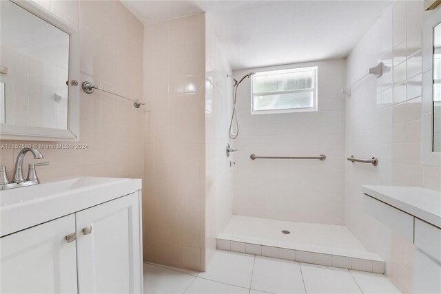 bathroom with tile patterned flooring, vanity, tile walls, and a tile shower