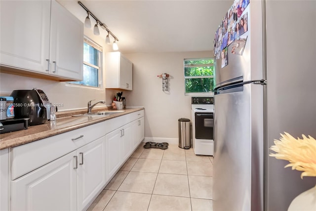 kitchen featuring white cabinets, light tile patterned floors, stainless steel refrigerator, sink, and white range