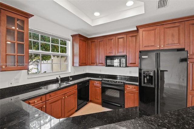 kitchen with a raised ceiling, light tile patterned floors, black appliances, dark stone counters, and sink