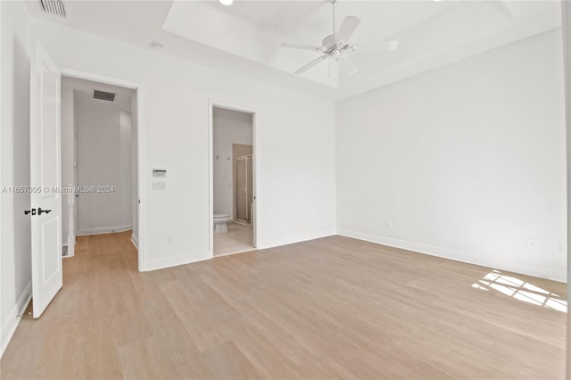 unfurnished bedroom with connected bathroom, a tray ceiling, ceiling fan, and light wood-type flooring