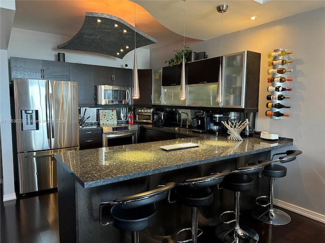 kitchen featuring dark stone countertops, backsplash, stainless steel appliances, kitchen peninsula, and dark hardwood / wood-style floors