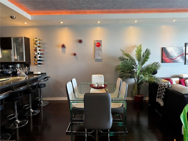 dining area with a tray ceiling, indoor bar, and dark hardwood / wood-style flooring