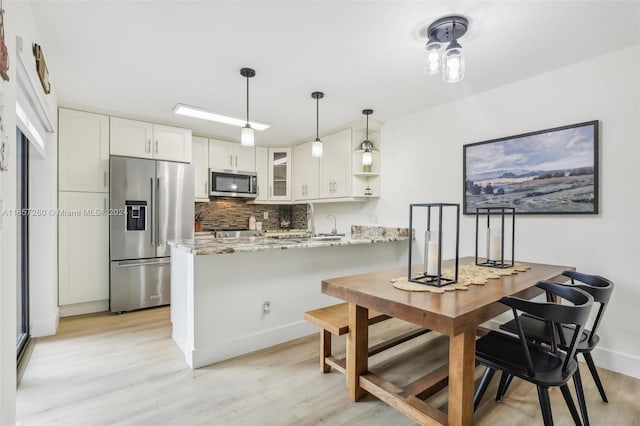 kitchen featuring kitchen peninsula, light stone countertops, white cabinets, appliances with stainless steel finishes, and light hardwood / wood-style floors