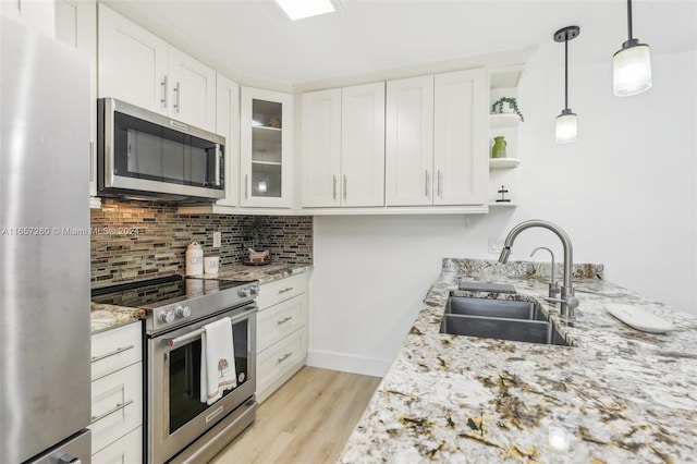 kitchen with sink, light wood-type flooring, hanging light fixtures, white cabinetry, and stainless steel appliances