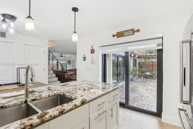 kitchen with hanging light fixtures, sink, fridge with ice dispenser, white cabinets, and light hardwood / wood-style floors