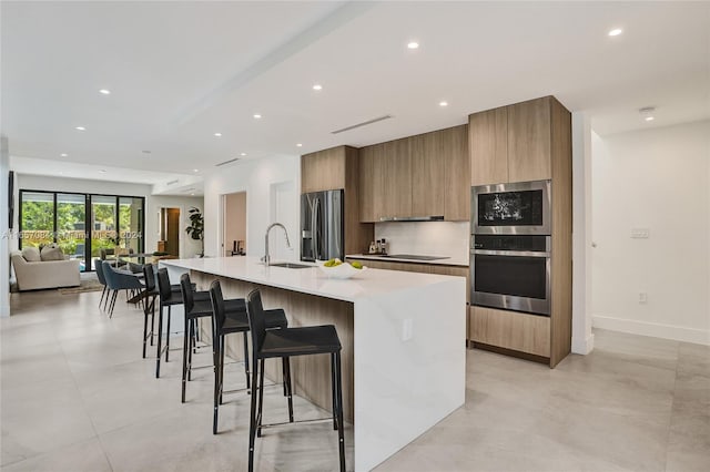 kitchen featuring backsplash, stainless steel appliances, a large island with sink, sink, and a kitchen bar