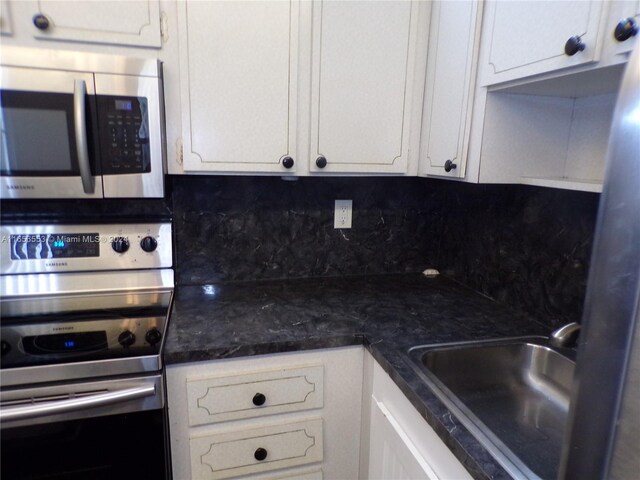 kitchen with dark stone counters, white cabinetry, sink, decorative backsplash, and appliances with stainless steel finishes