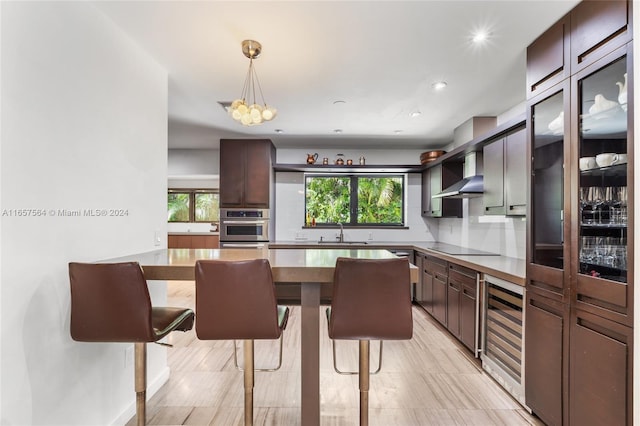 kitchen featuring black electric stovetop, stainless steel oven, dark brown cabinets, sink, and hanging light fixtures