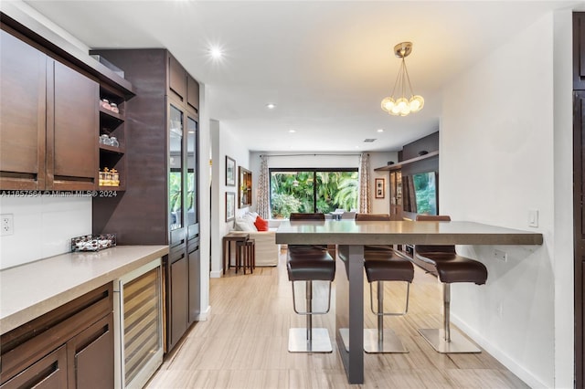 kitchen with a kitchen breakfast bar, dark brown cabinetry, decorative light fixtures, an inviting chandelier, and wine cooler