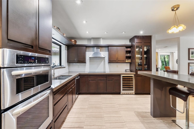 kitchen featuring sink, hanging light fixtures, beverage cooler, stainless steel appliances, and a kitchen bar