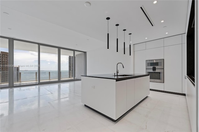 kitchen with pendant lighting, sink, white cabinetry, a water view, and an island with sink