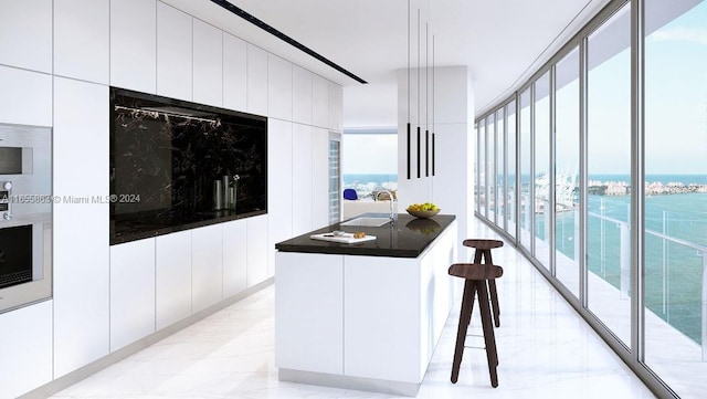 kitchen with a water view, a breakfast bar, sink, and white cabinetry