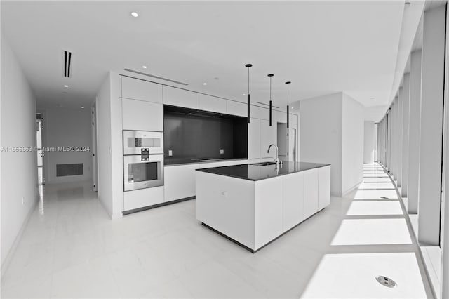 kitchen with decorative light fixtures, white cabinets, an island with sink, and sink