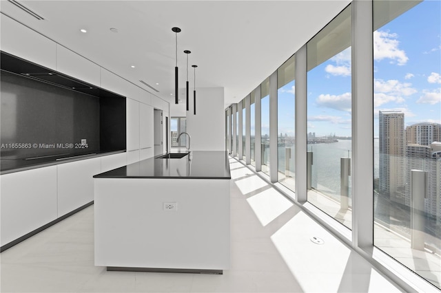 kitchen featuring a water view, decorative light fixtures, sink, an island with sink, and white cabinets