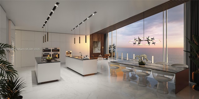 interior space with white cabinetry, hanging light fixtures, a kitchen island, and a water view