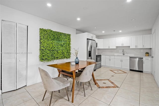 kitchen featuring stainless steel appliances, light tile patterned floors, tasteful backsplash, white cabinets, and sink