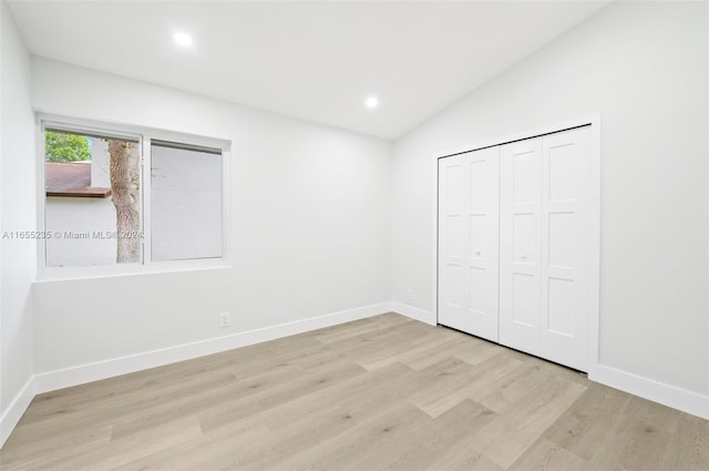 unfurnished bedroom with a closet, lofted ceiling, and light wood-type flooring