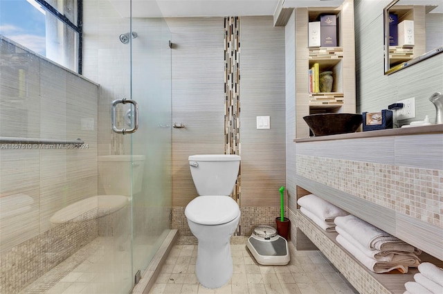 bathroom featuring tile walls, toilet, and a shower with shower door