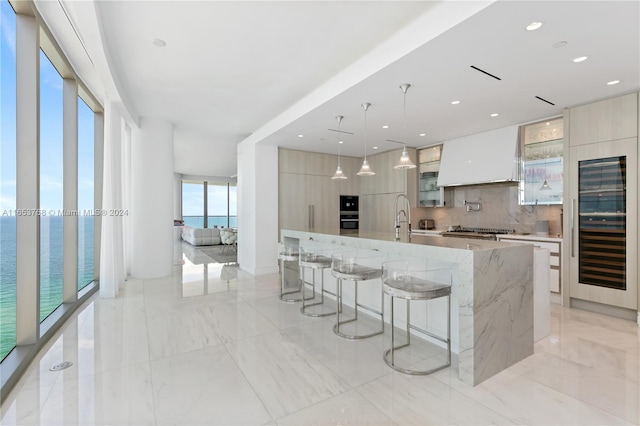 kitchen with a large island with sink, a water view, stainless steel gas cooktop, beverage cooler, and light stone counters