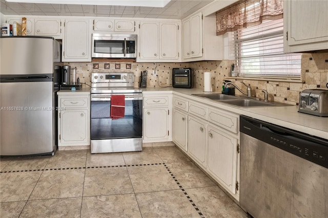 kitchen featuring white cabinets, sink, decorative backsplash, light tile patterned floors, and stainless steel appliances