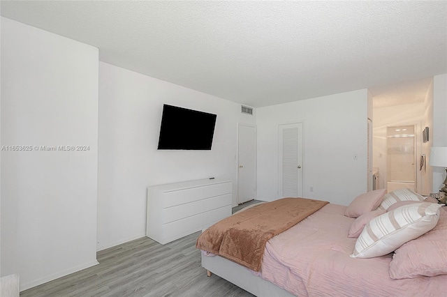 bedroom with light wood-type flooring, a closet, ensuite bath, and a textured ceiling