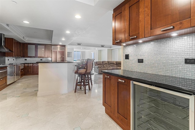 kitchen with a kitchen breakfast bar, wall chimney exhaust hood, wine cooler, and tasteful backsplash