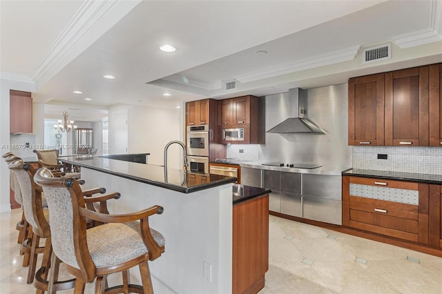 kitchen featuring decorative backsplash, a kitchen island with sink, wall chimney range hood, and stainless steel appliances