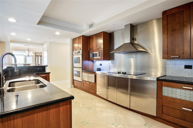 kitchen with sink, wall chimney exhaust hood, stainless steel appliances, backsplash, and an inviting chandelier