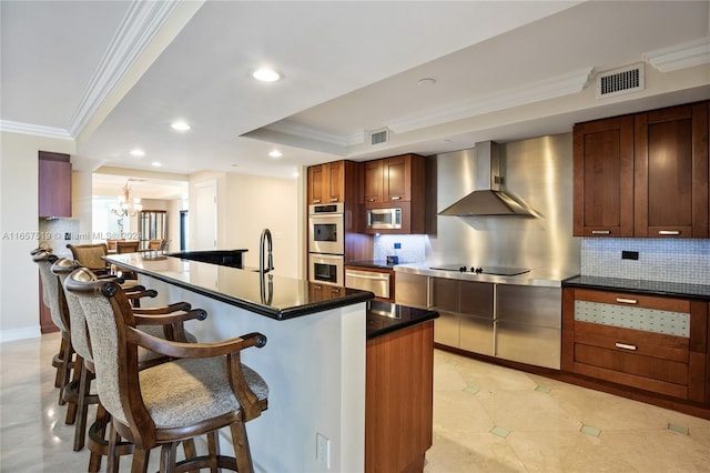 kitchen featuring tasteful backsplash, stainless steel appliances, crown molding, a kitchen island with sink, and wall chimney range hood