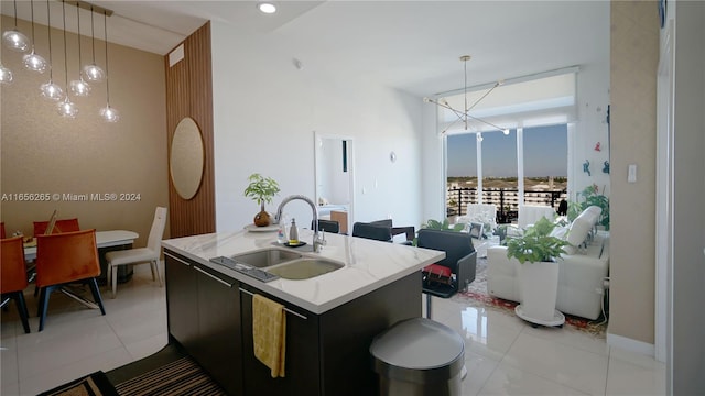 kitchen with light tile patterned floors, decorative light fixtures, a kitchen island with sink, sink, and a notable chandelier