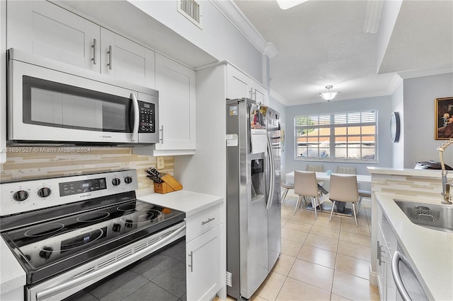 kitchen with white cabinetry, appliances with stainless steel finishes, a textured ceiling, light tile patterned floors, and ornamental molding