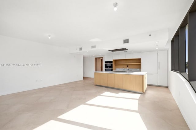 kitchen with dobule oven black, visible vents, light countertops, a center island, and modern cabinets