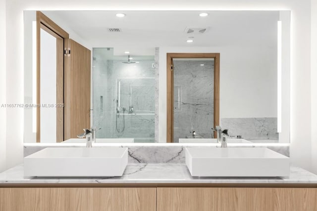 full bath with double vanity, a marble finish shower, visible vents, and a sink