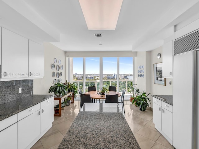 kitchen featuring dark stone counters, paneled refrigerator, white cabinetry, and a skylight