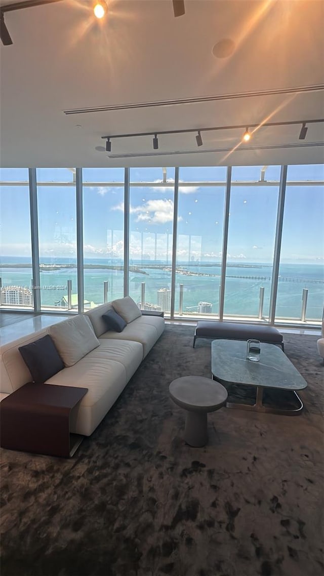 living room featuring rail lighting, a water view, and floor to ceiling windows