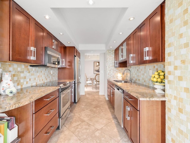 kitchen with stainless steel appliances, light stone counters, a tray ceiling, and sink