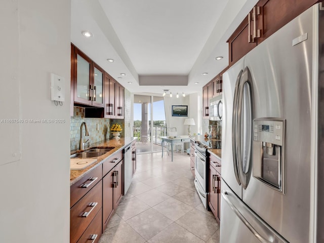 kitchen featuring sink, light stone counters, a tray ceiling, light tile patterned floors, and appliances with stainless steel finishes