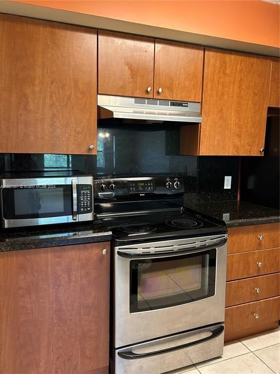 kitchen with dark stone counters, stainless steel appliances, light tile patterned flooring, and decorative backsplash