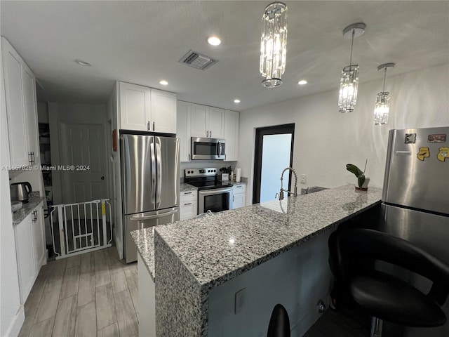 kitchen with a notable chandelier, stone counters, kitchen peninsula, appliances with stainless steel finishes, and light hardwood / wood-style floors