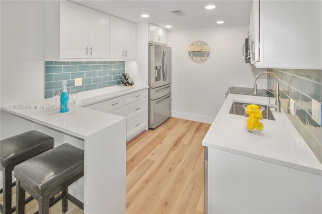 kitchen with backsplash, white cabinets, sink, appliances with stainless steel finishes, and light hardwood / wood-style floors