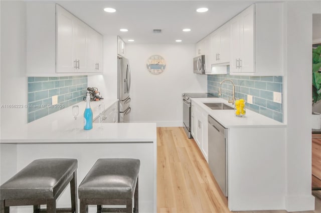 kitchen with a kitchen breakfast bar, stainless steel appliances, sink, light hardwood / wood-style flooring, and white cabinetry