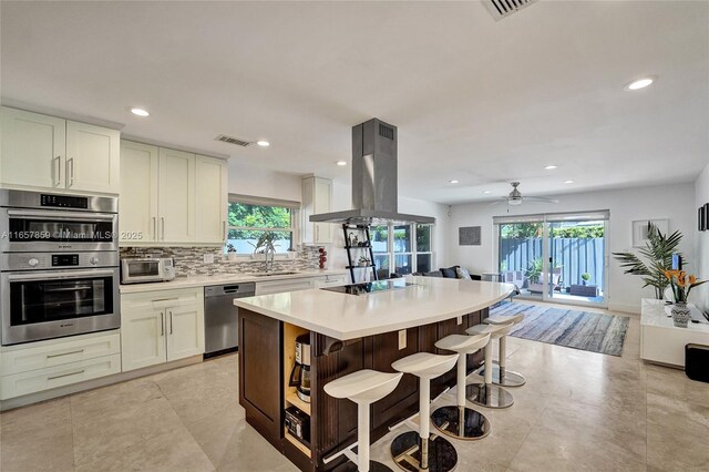 kitchen featuring ceiling fan, stainless steel appliances, a kitchen island, island range hood, and white cabinets