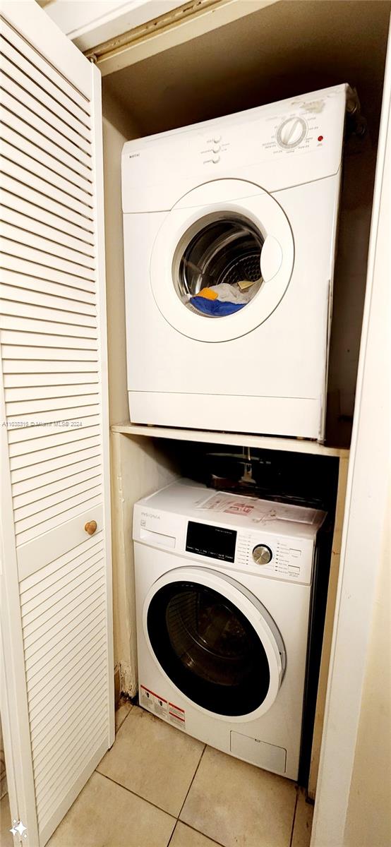 clothes washing area featuring light tile patterned flooring and stacked washing maching and dryer