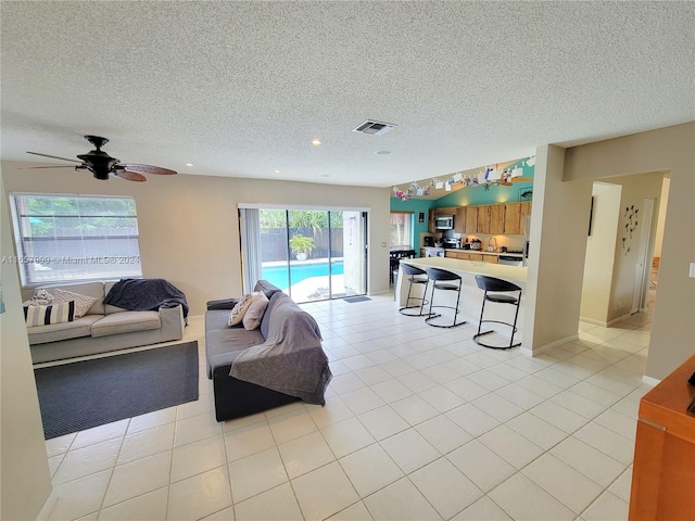 living area featuring light tile patterned flooring, visible vents, a textured ceiling, and a ceiling fan