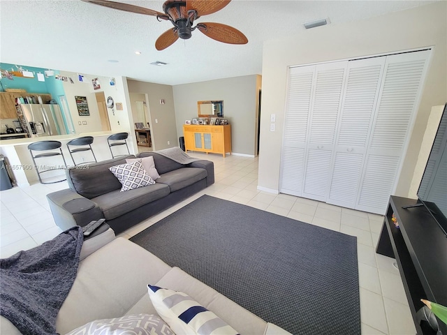 living area with light tile patterned floors, visible vents, a textured ceiling, and a ceiling fan