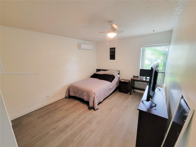 bedroom featuring a wall unit AC, a ceiling fan, baseboards, light wood finished floors, and a textured ceiling