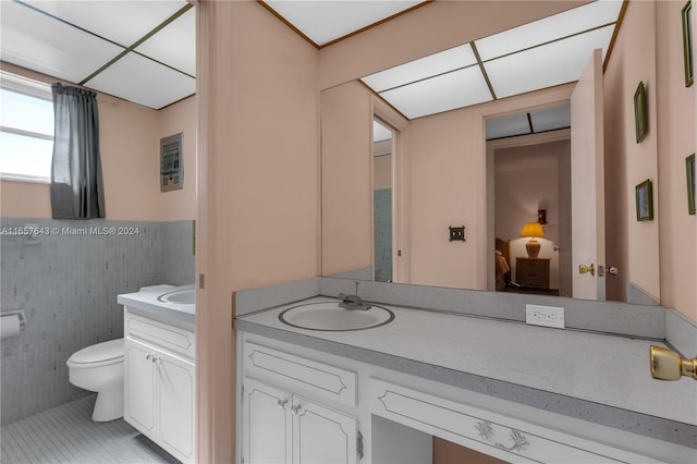 bathroom featuring tile patterned flooring, vanity, toilet, and tile walls